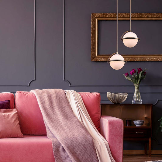 pink couch, with a  lighter pink blanket layed across it.  In front of a dark purple wall, two gold and opal pendants hanging from the ceiling