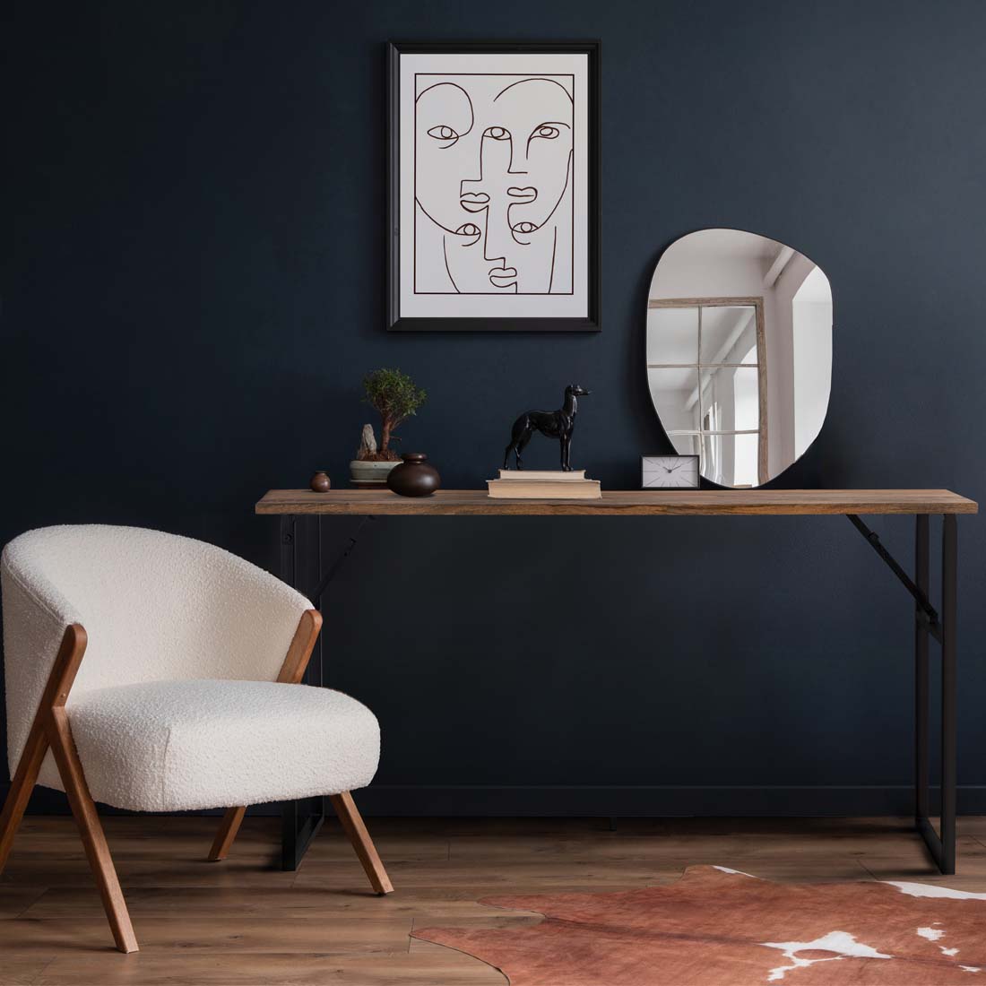 Load video: video showing a long console table with a wooden top and black iron legs.  With a cream chair.  Walls are painted a dark blue with an abstract art photo hung above the table.