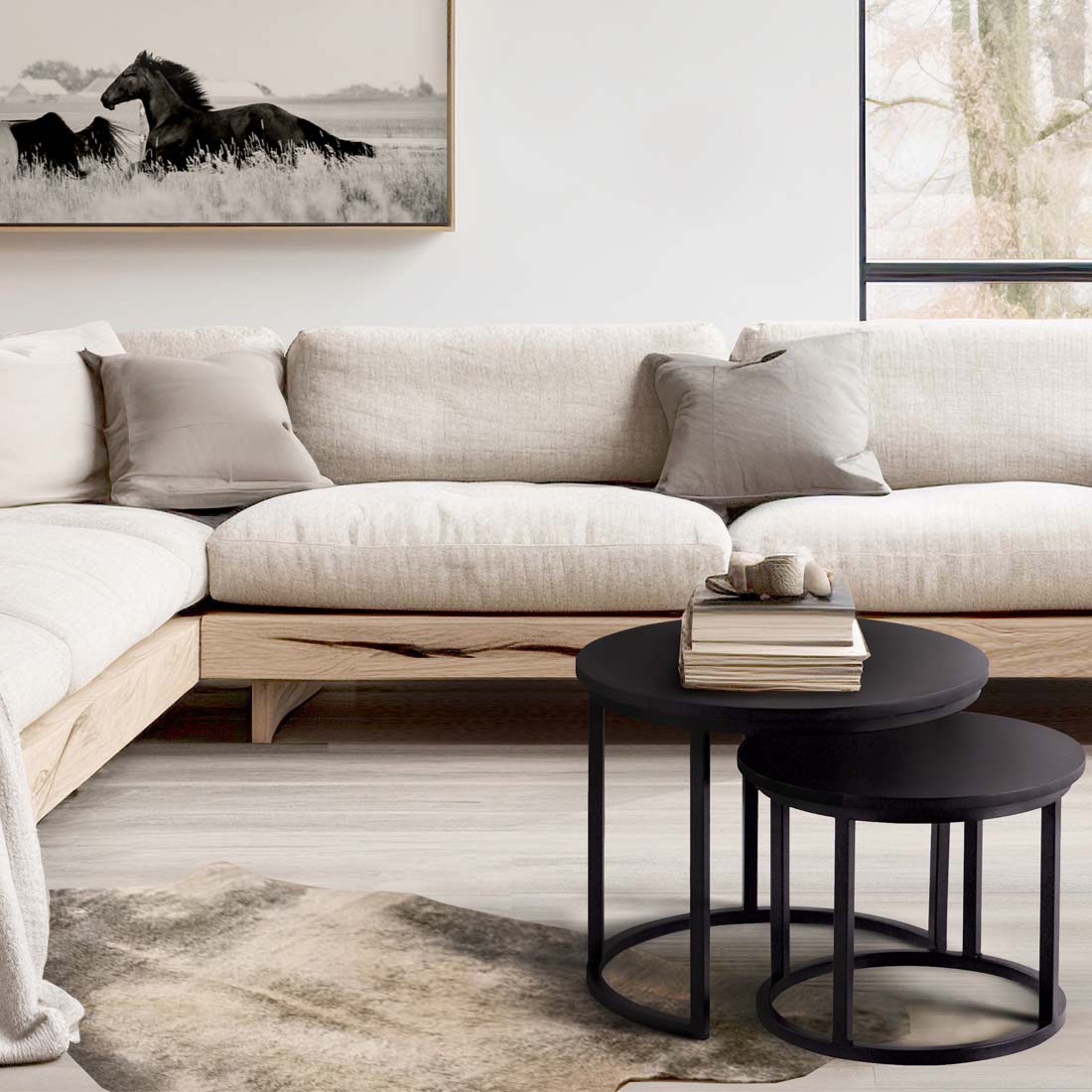 Load video: video showing two nested side tables in a black wood top surface and iron black legs, placed in a living room with a large cream sofa, and a art print hung on the wall of two black horses running